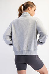 woman wearing a gray oversized sweatshirt with a high collar and ribbed hem, paired with gray bike shorts