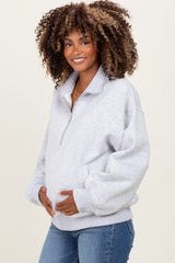 woman wearing a gray maternity pullover with a half zipper and holding her baby bump