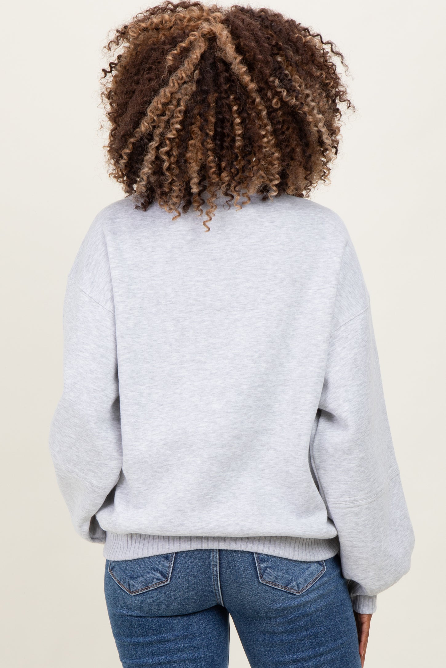 woman wearing a light gray maternity sweatshirt with a relaxed fit, showing the back view and paired with denim jeans