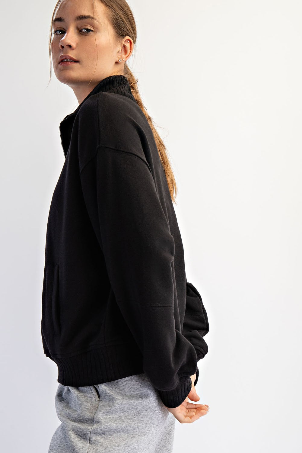 woman wearing a black pullover sweatshirt with a high collar and side pockets, styled with gray sweatpants