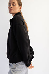 woman wearing a black pullover sweatshirt with a high collar and side pockets, styled with gray sweatpants