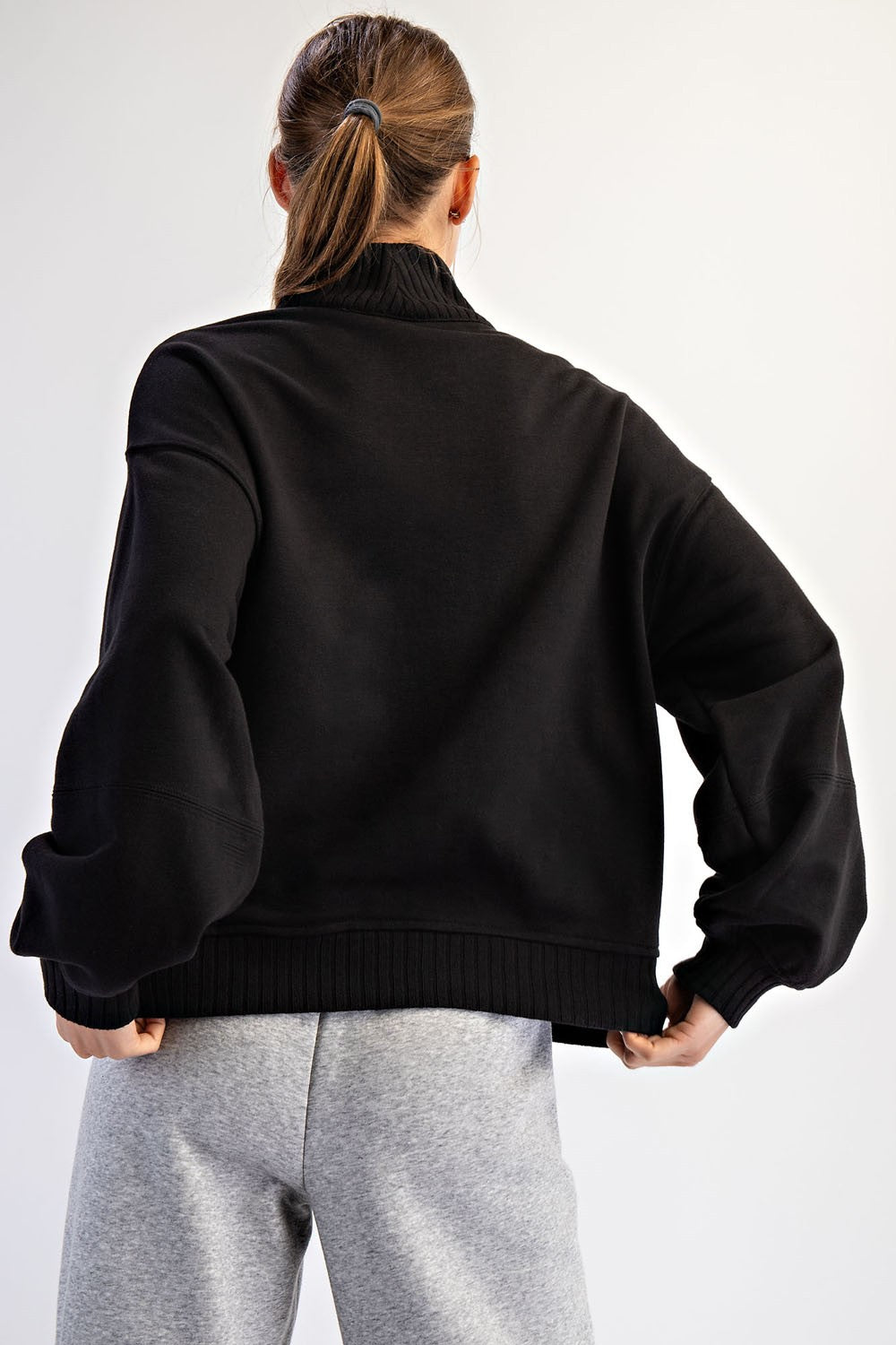 woman wearing a black oversized sweater with balloon sleeves and a high collar, viewed from the back