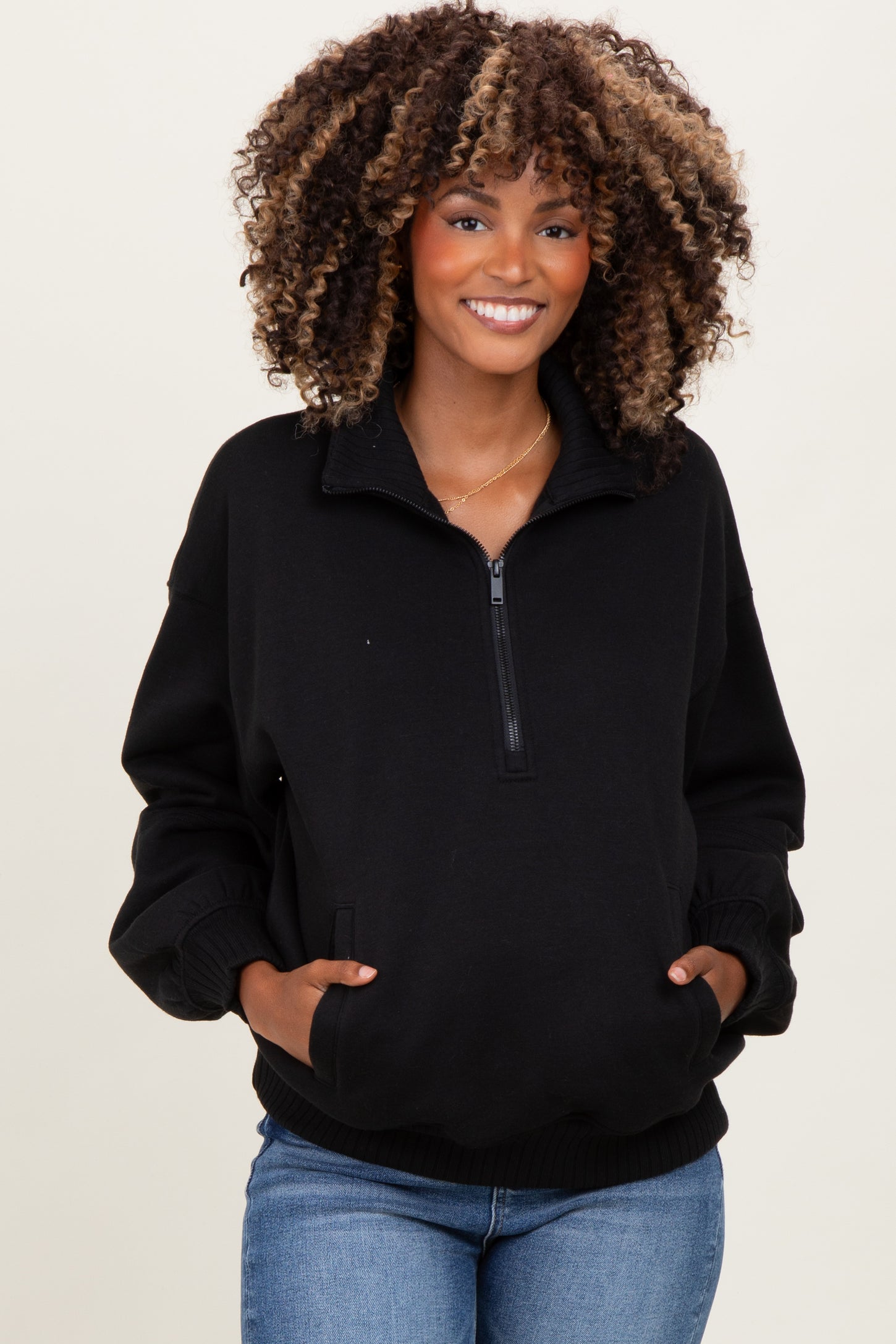 woman wearing a black maternity quarter-zip sweatshirt with side pockets and a relaxed fit, showing her baby bump