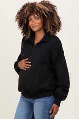 woman wearing a black maternity pullover with a zip front and holding her baby bump