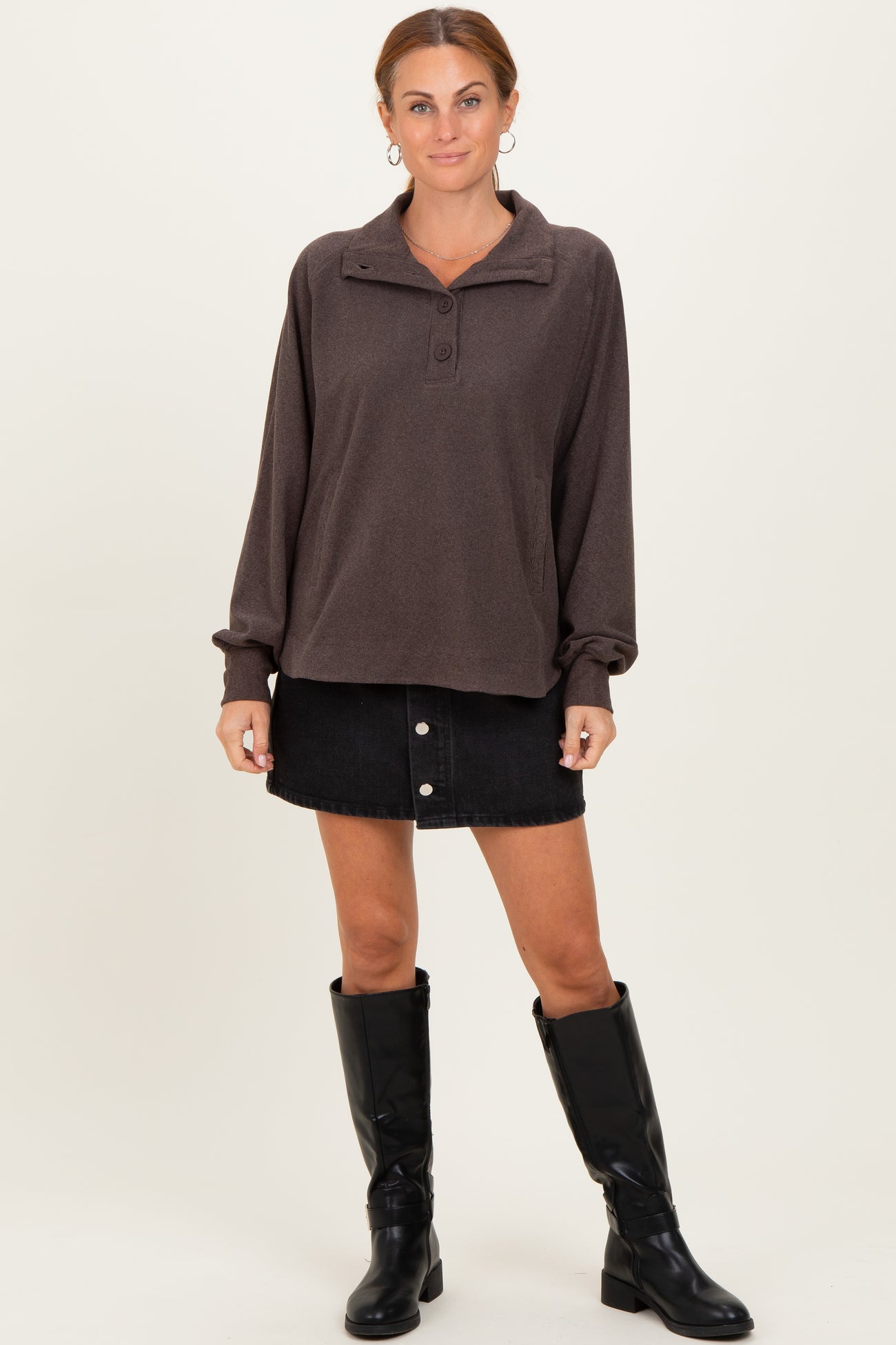 woman wearing a brown pullover sweatshirt with a collar and buttons, paired with a black denim skirt and black knee-high boots