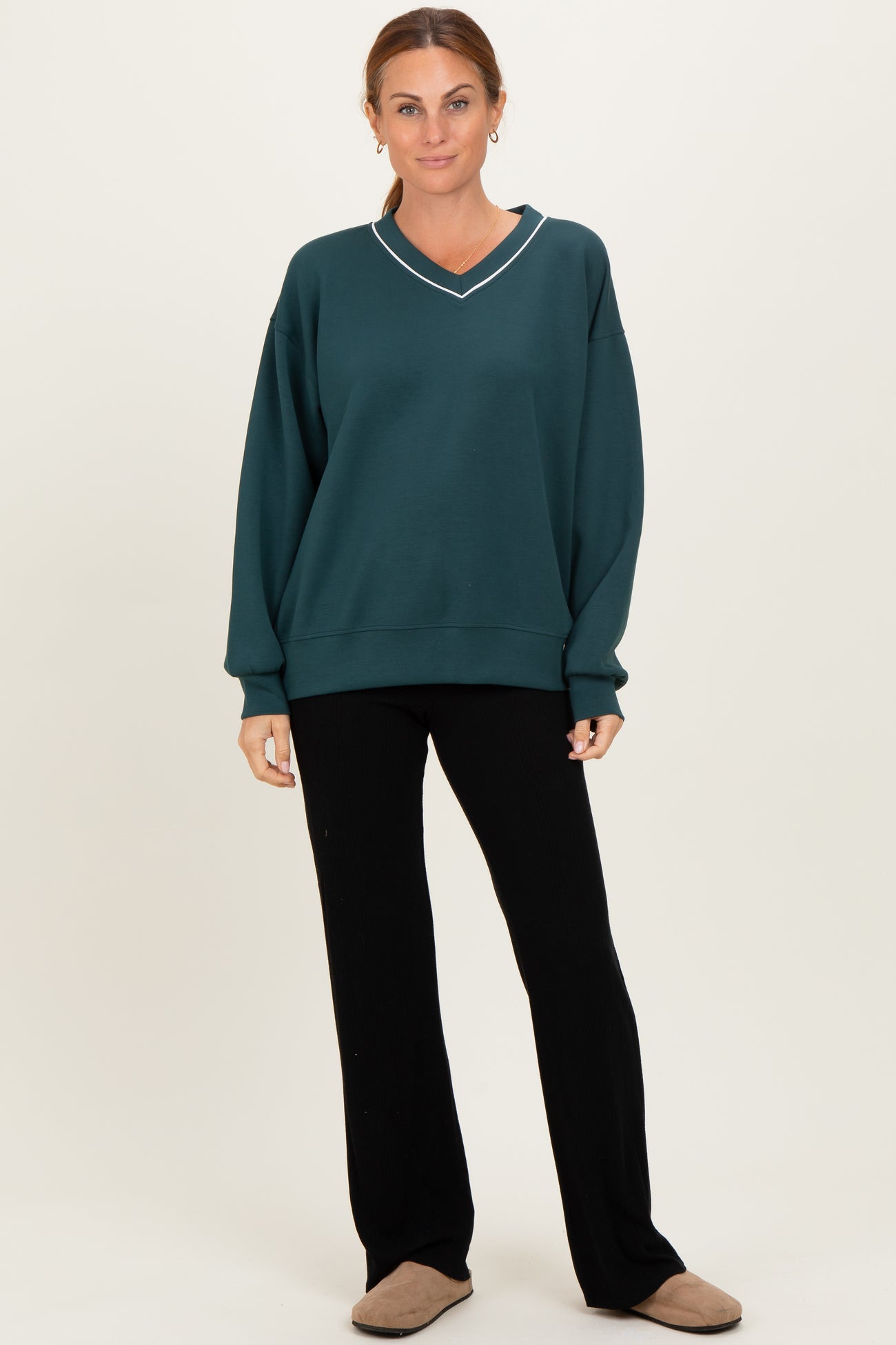 woman wearing a dark green oversized sweatshirt with a v-neck and white trim paired with black wide-leg pants