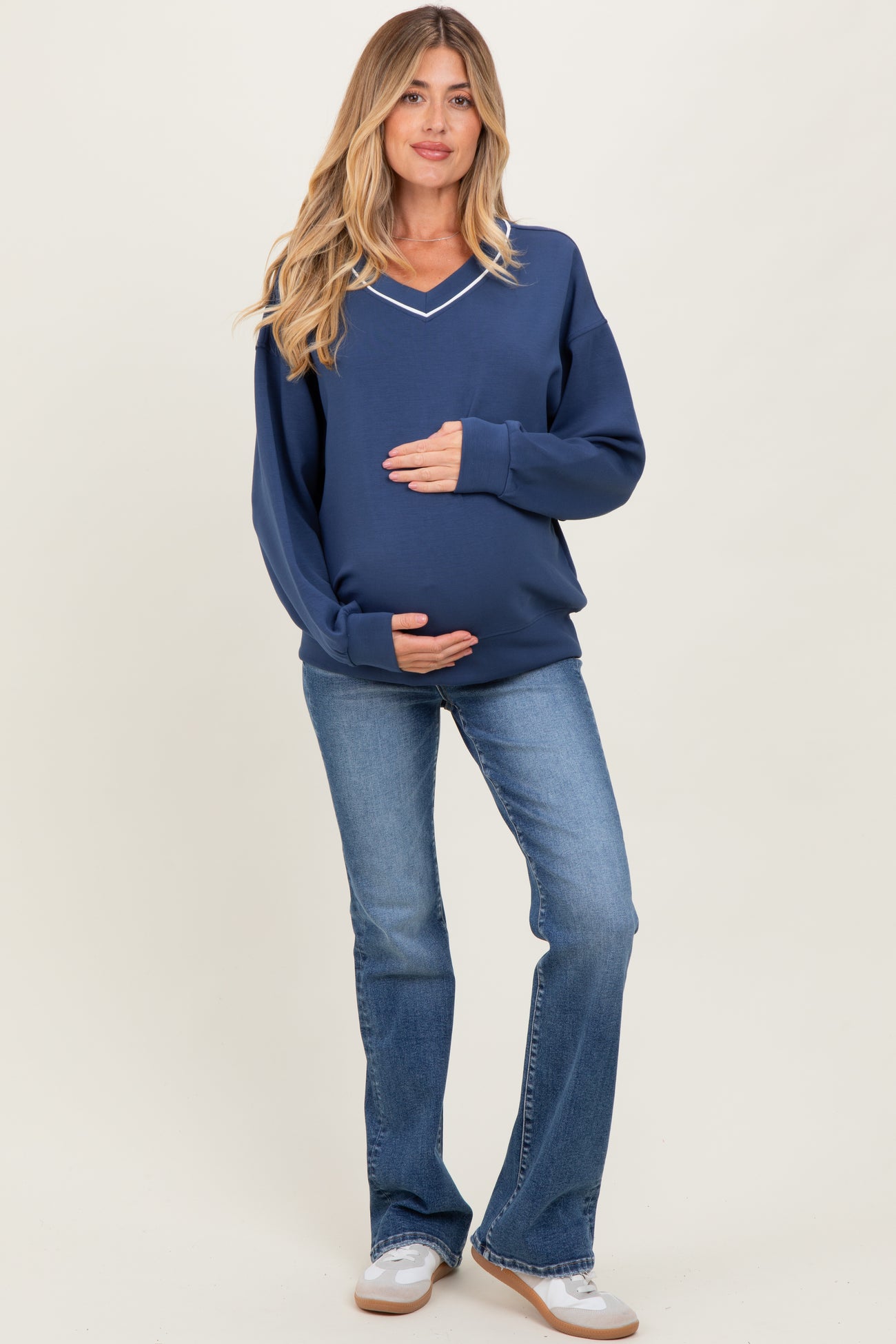 woman wearing a navy v-neck maternity sweatshirt and holding her baby bump, paired with light blue flared jeans
