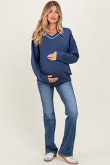 woman wearing a navy v-neck maternity sweatshirt and holding her baby bump, paired with light blue flared jeans