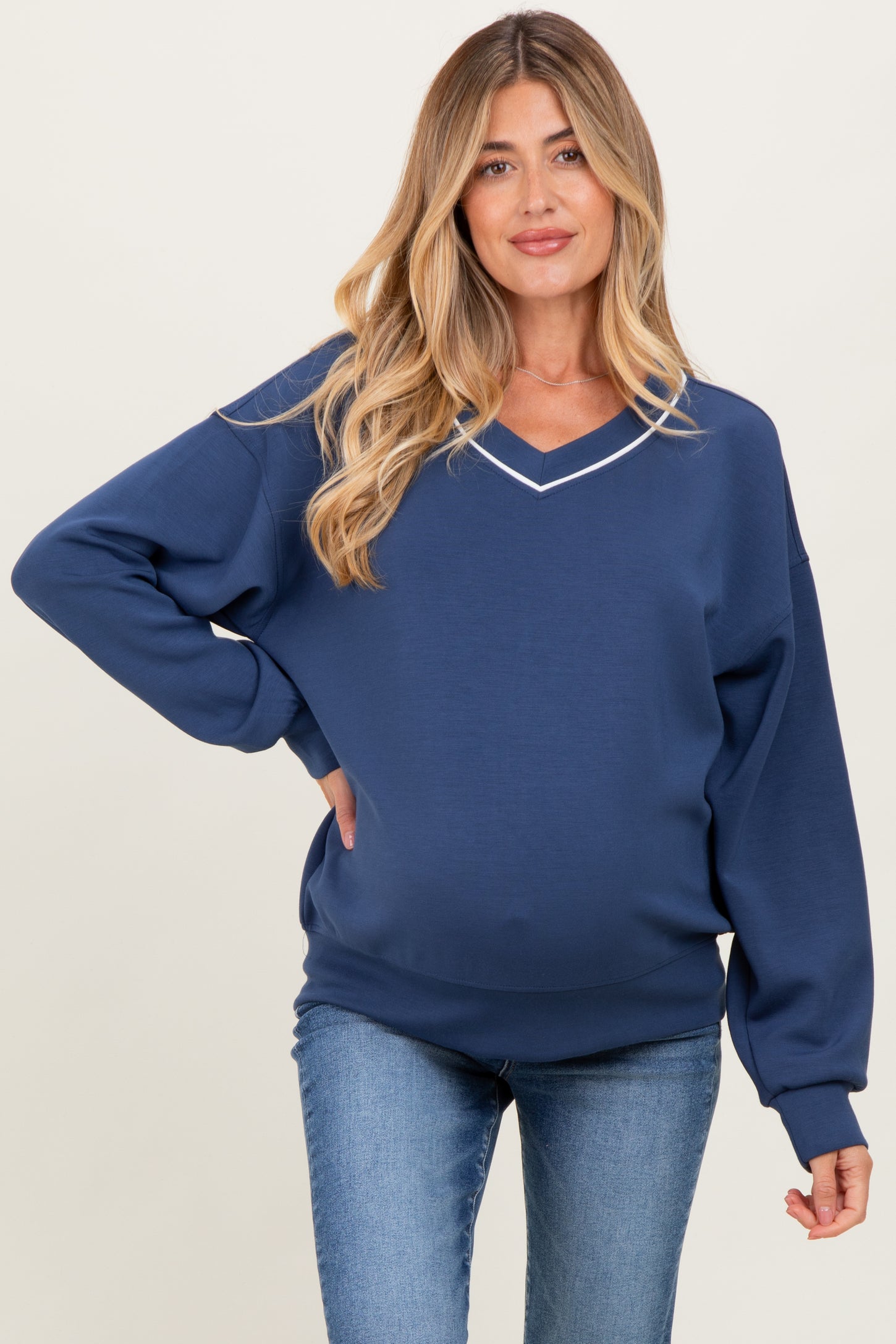 woman wearing a navy blue maternity sweatshirt with a v-neck and white collar detail, showing her baby bump