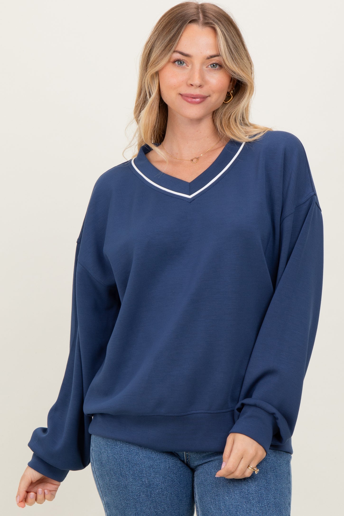 woman wearing a navy oversized sweatshirt with a v-neck and white trim details, posing casually