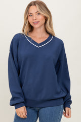 woman wearing a navy blue oversized sweatshirt with a v-neck and white trim details, styled with blue jeans