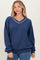woman wearing a navy blue oversized sweatshirt with a v-neck and white trim details, styled with blue jeans