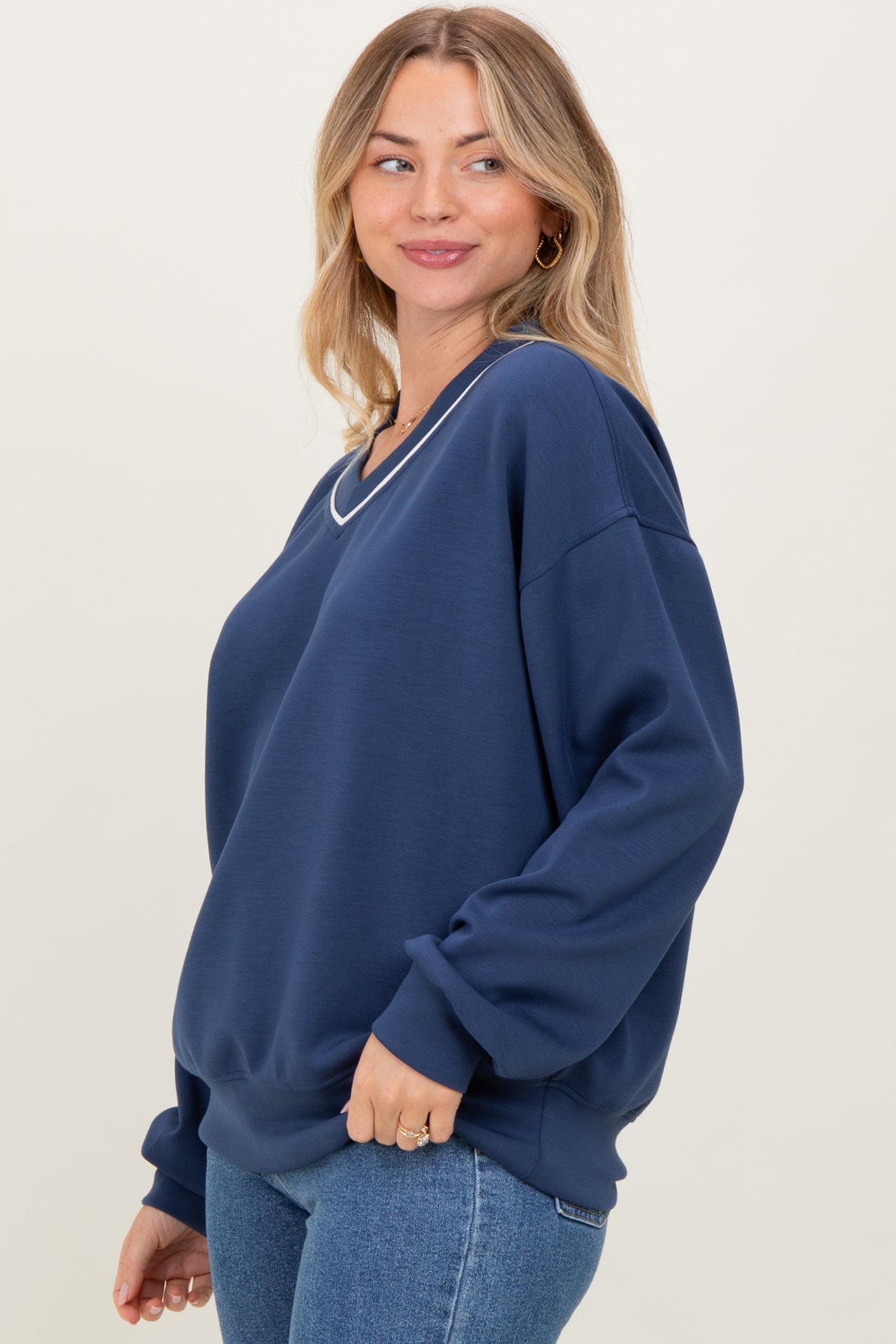 woman wearing a navy blue oversized sweatshirt with a v-neck and long sleeves, styled with blue jeans