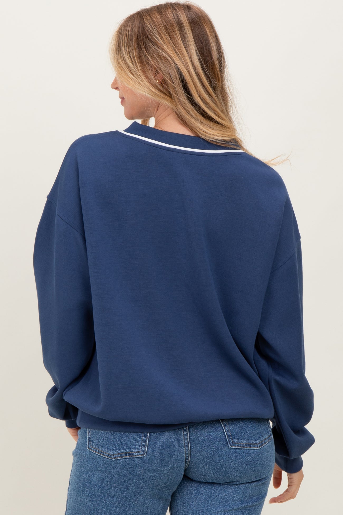 woman wearing a navy blue oversized sweatshirt with a white collar detail, view from the back