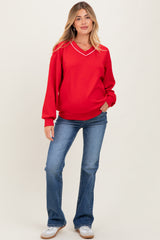 woman wearing a red maternity sweatshirt with a v-neckline and white piping, paired with blue flared jeans