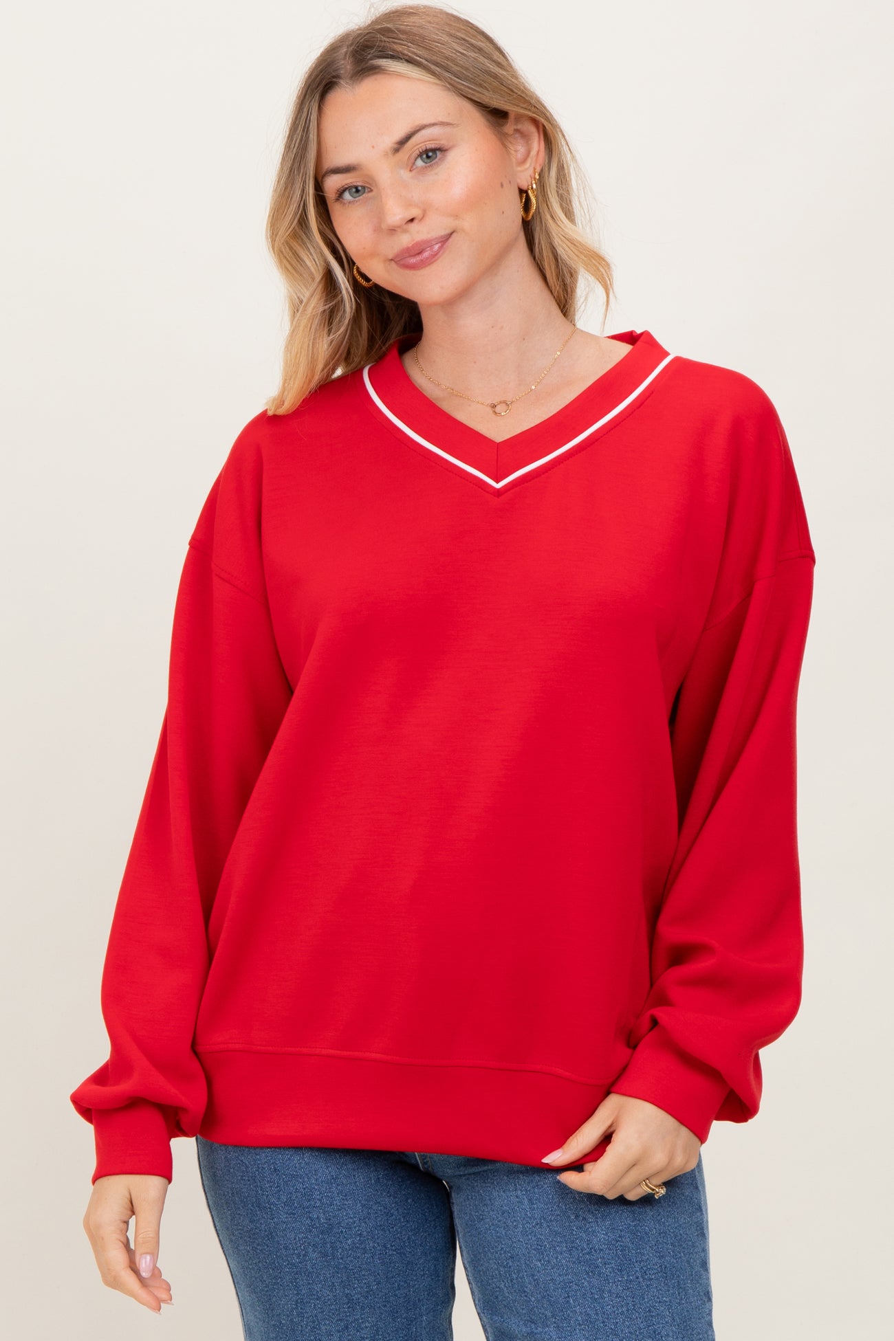 woman wearing a bright red oversized sweatshirt with a v-neckline and white trim, paired with blue jeans