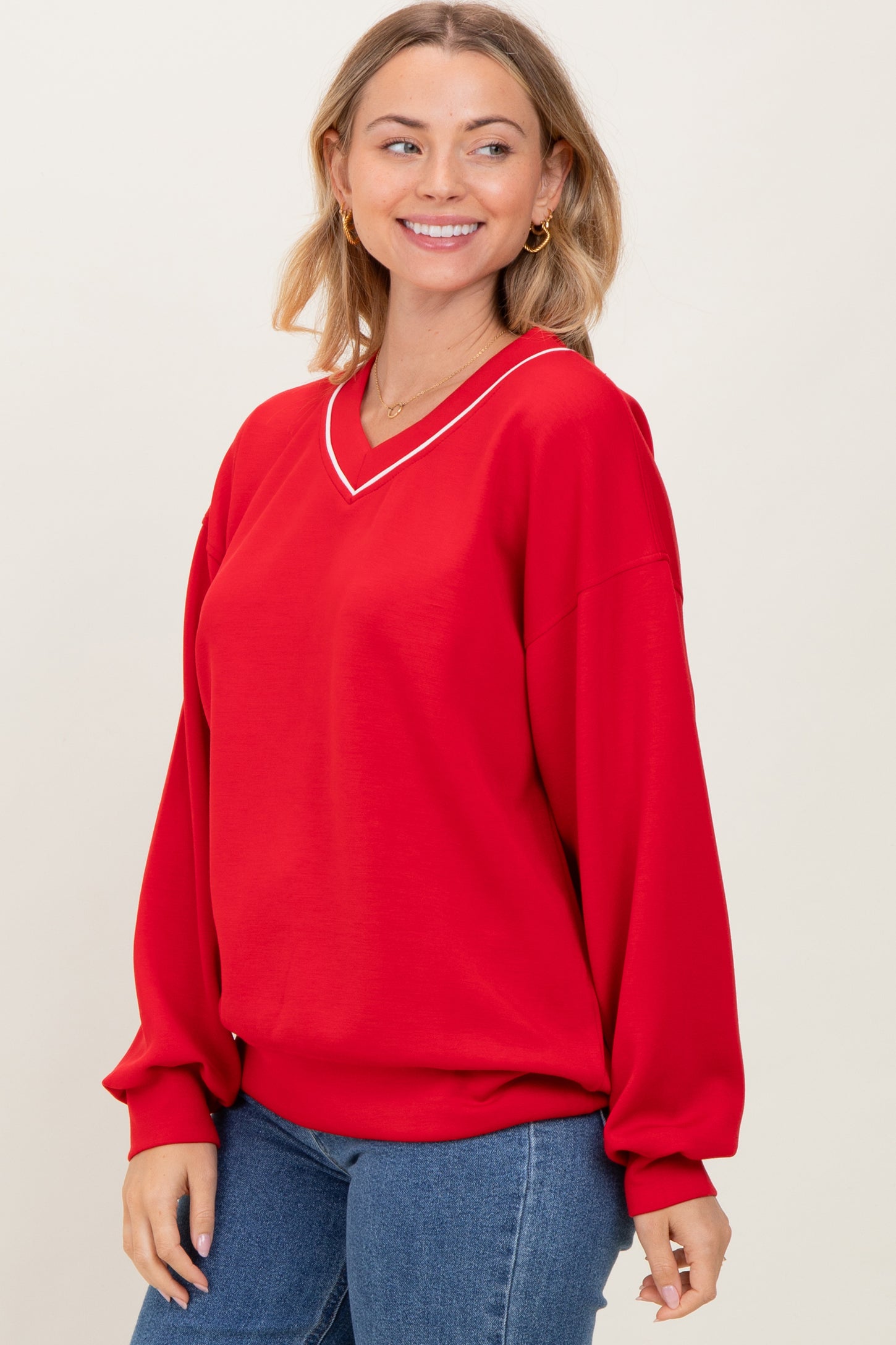woman wearing a bright red oversized sweatshirt with a v-neckline and white trim, paired with blue jeans