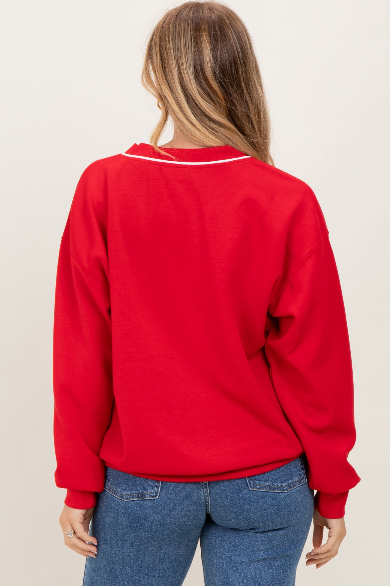 woman wearing a red oversized sweatshirt with white collar detailing, showing the back view