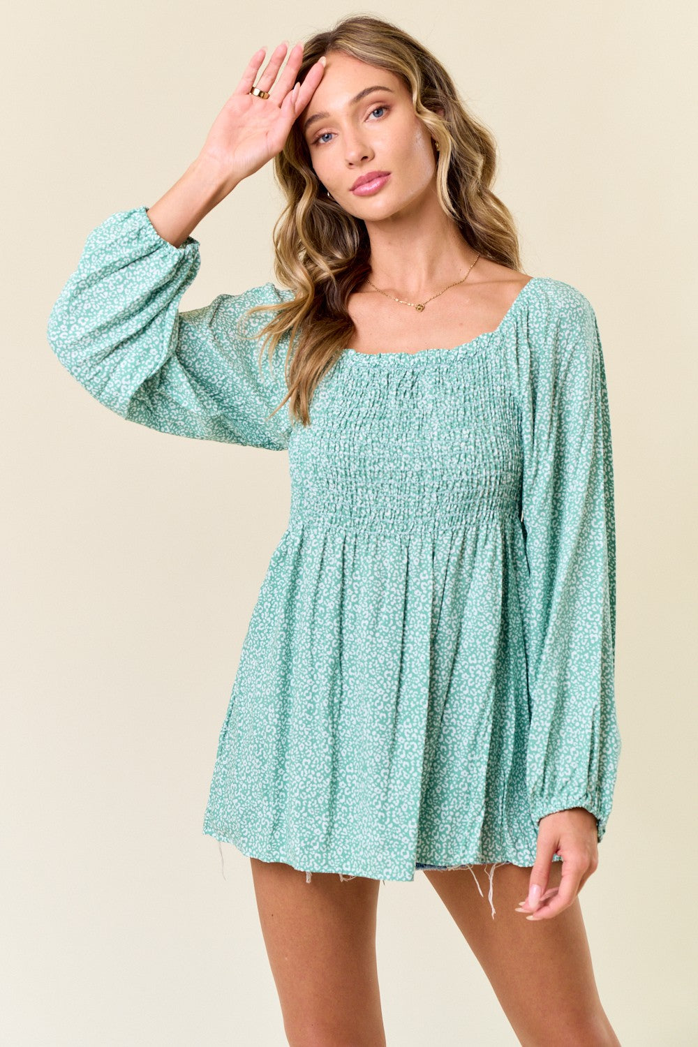 woman wearing a mint green smocked mini dress with long puff sleeves and floral pattern