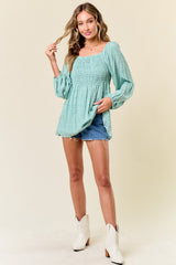 woman wearing a mint green smocked top with long sleeves and denim shorts, styled with white cowboy boots