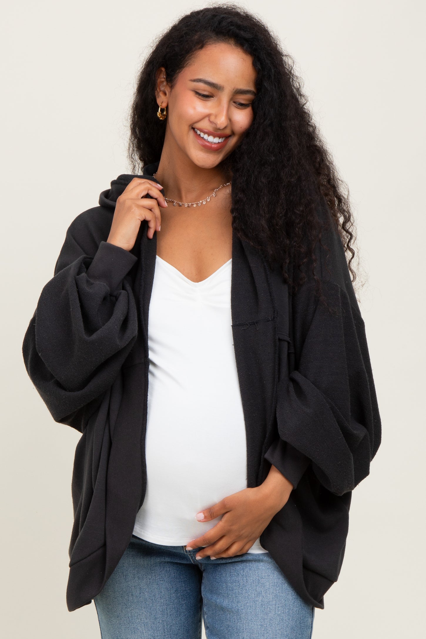 woman wearing a black oversized maternity hoodie and holding her baby bump, styled with a white top and jeans