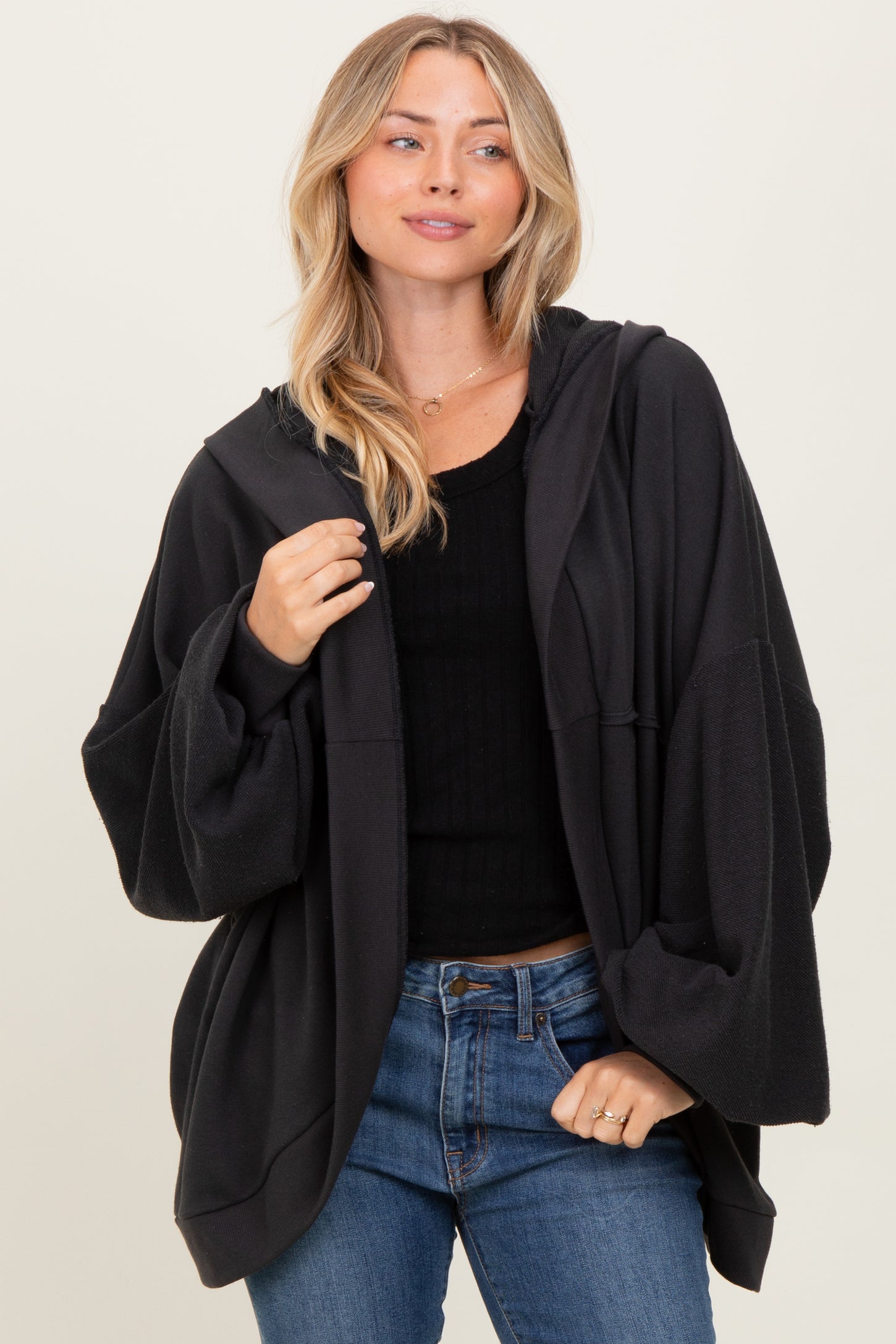woman wearing a black oversized hooded sweatshirt with wide sleeves and a front pocket, styled with blue jeans