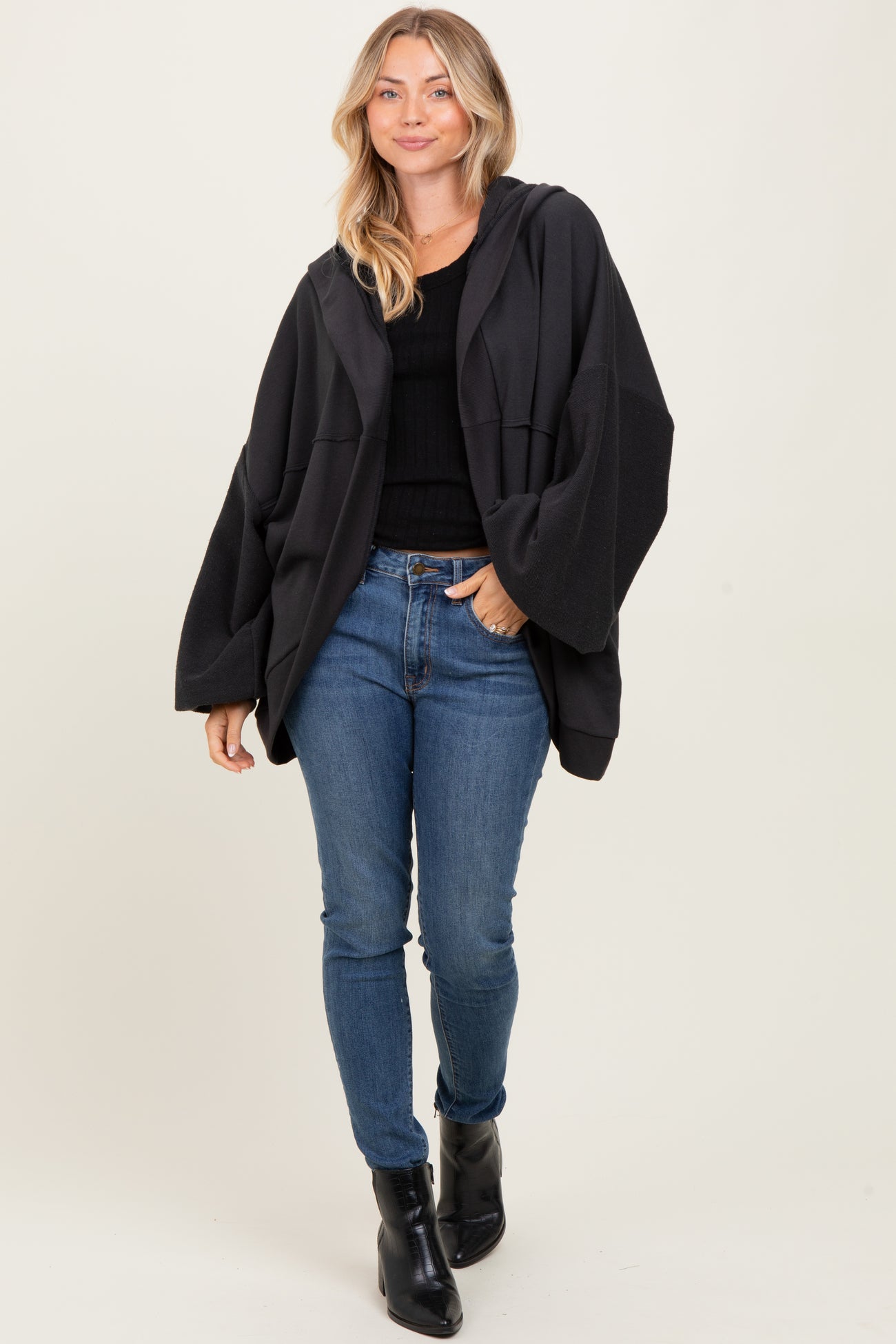 woman wearing a black oversized hoodie over a fitted black top and blue skinny jeans, with black ankle boots
