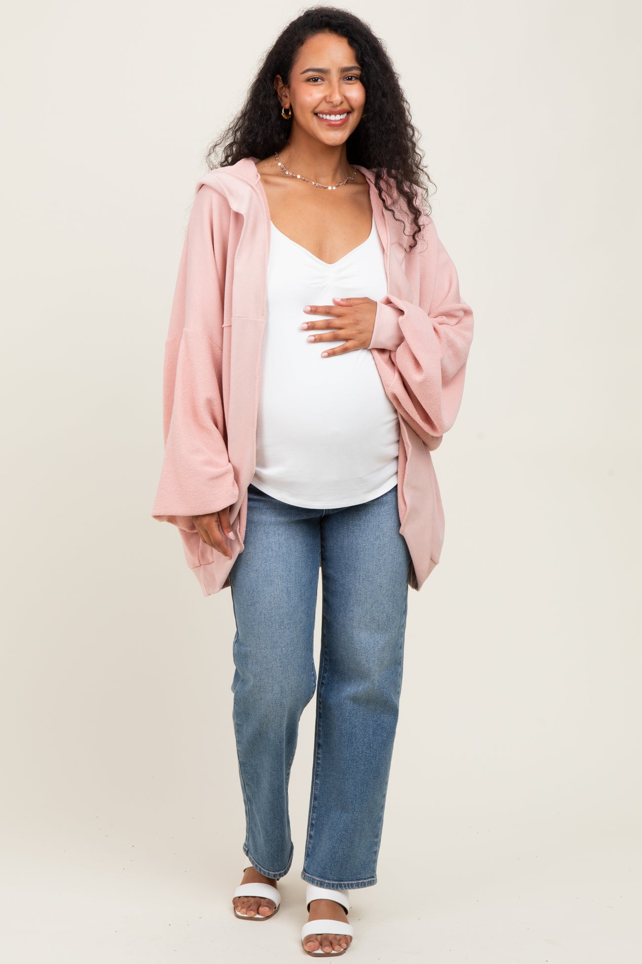 woman wearing a light pink maternity hoodie over a white top, paired with jeans and showing her baby bump