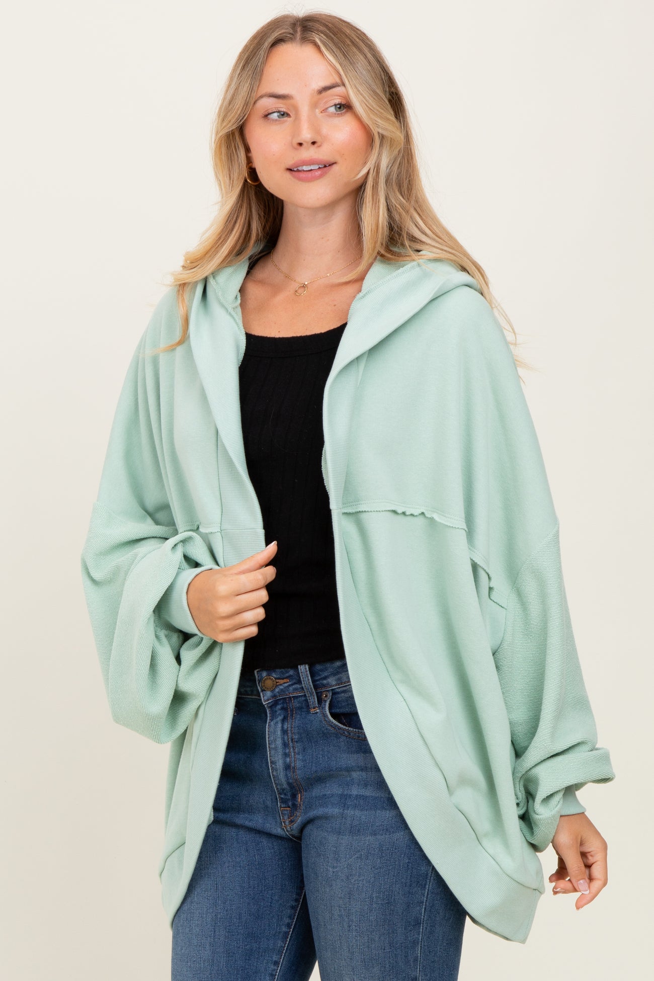 woman wearing a mint green oversized hooded cardigan over a black top and blue jeans