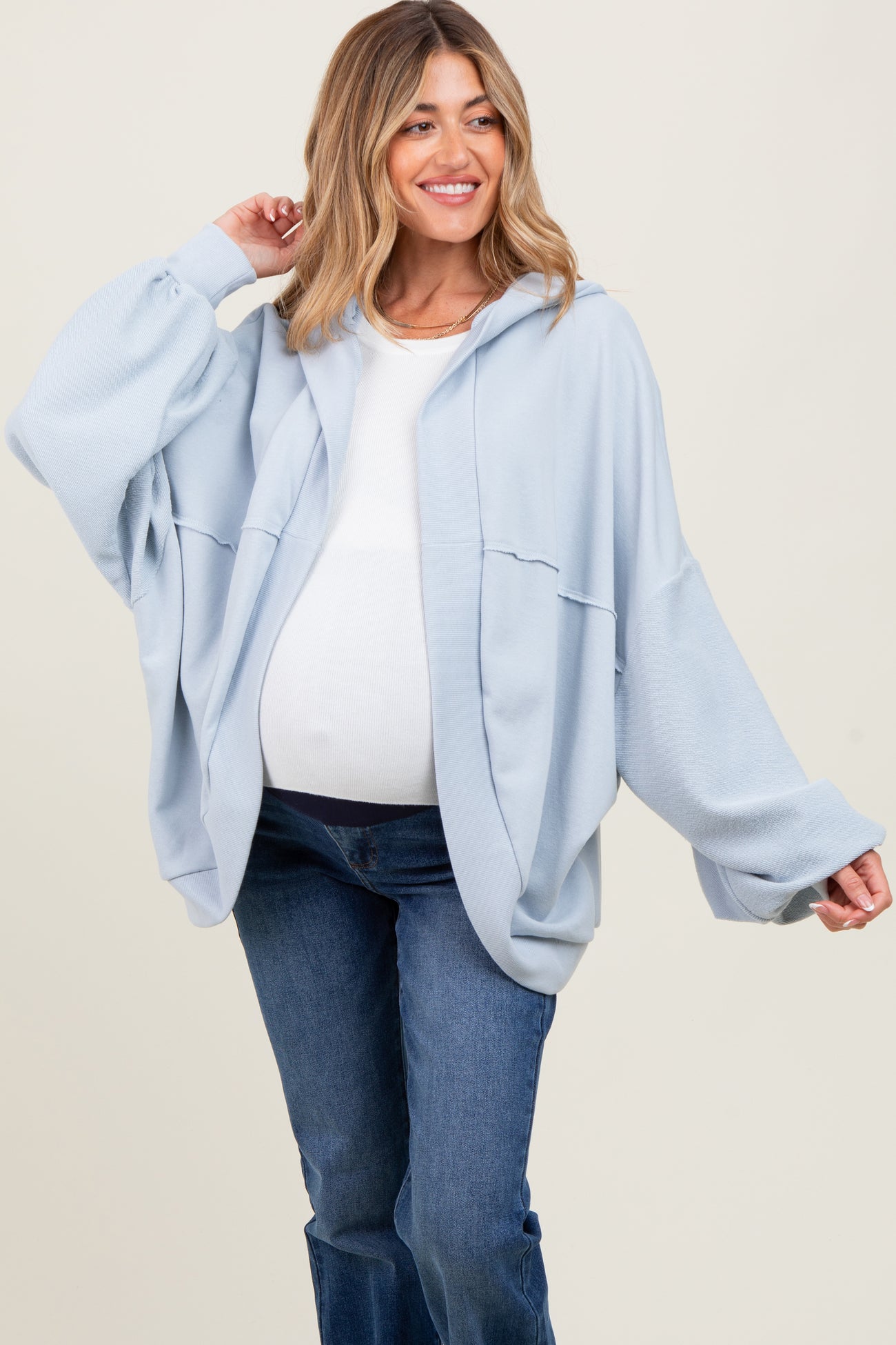 woman wearing a light blue oversized hooded maternity jacket with a white top and showing her baby bump