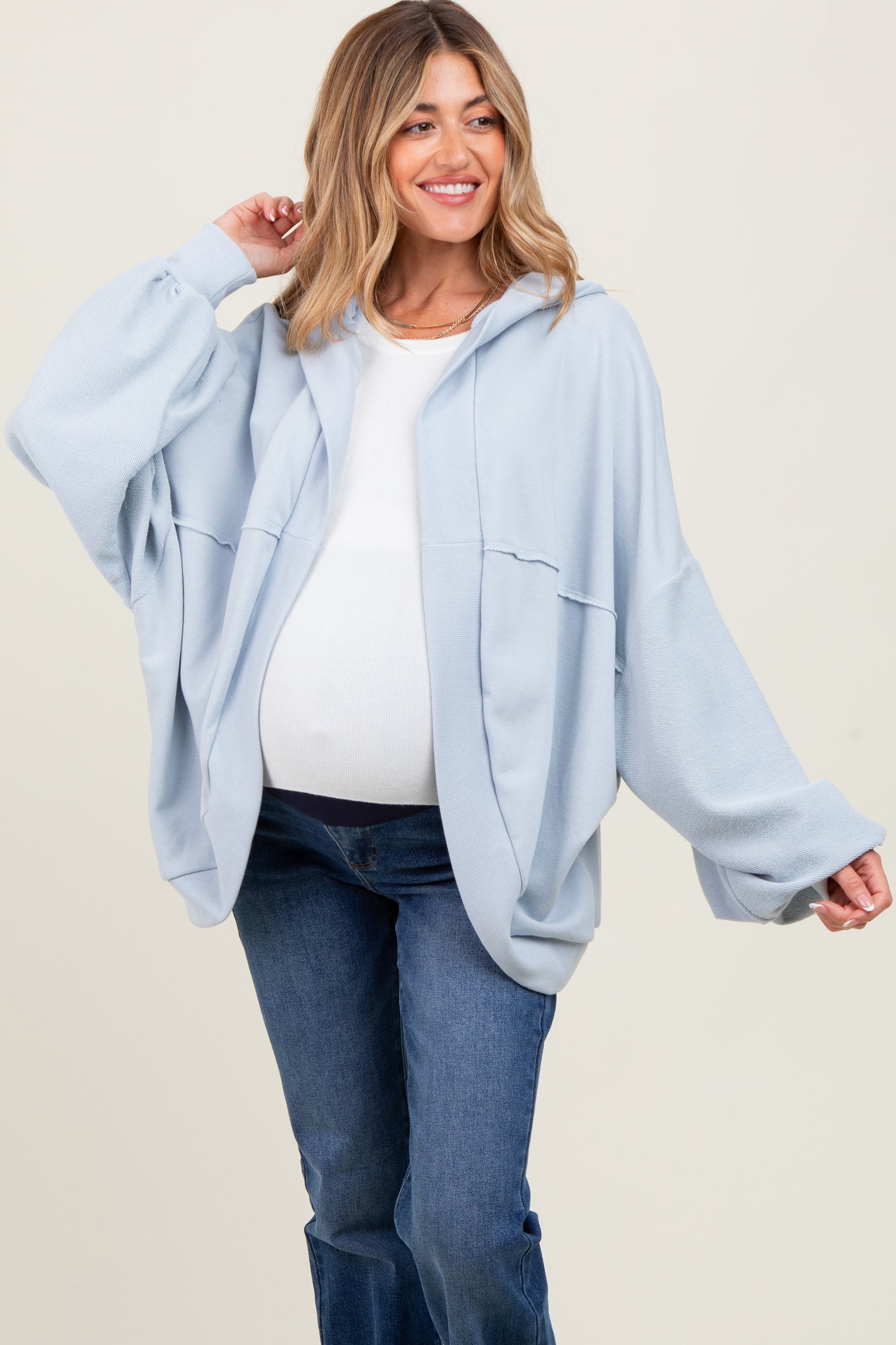 woman wearing a light blue oversized hooded maternity jacket with a white top and showing her baby bump