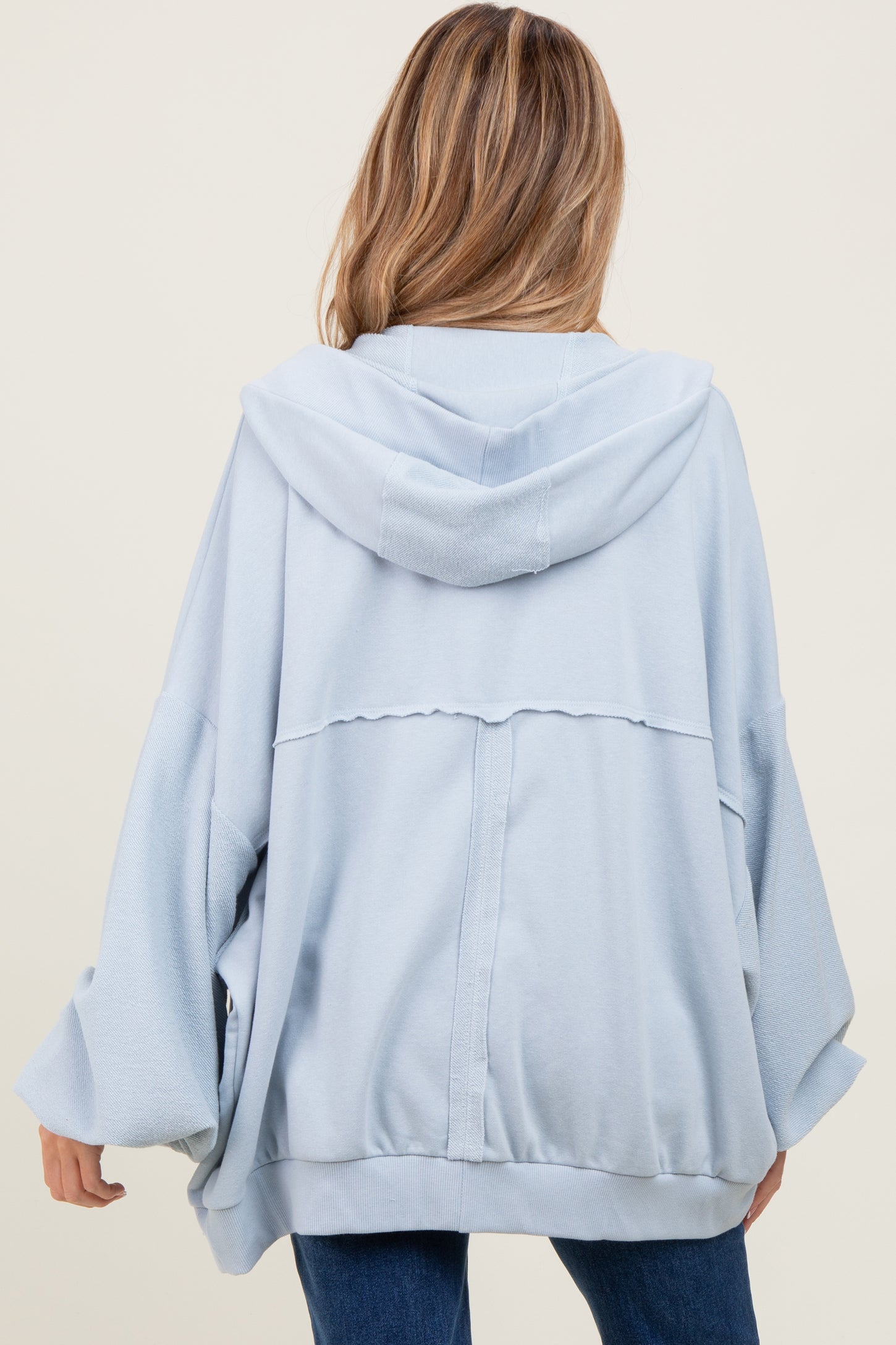 woman wearing a light blue oversized maternity hoodie with a hood and loose sleeves, showing the back view
