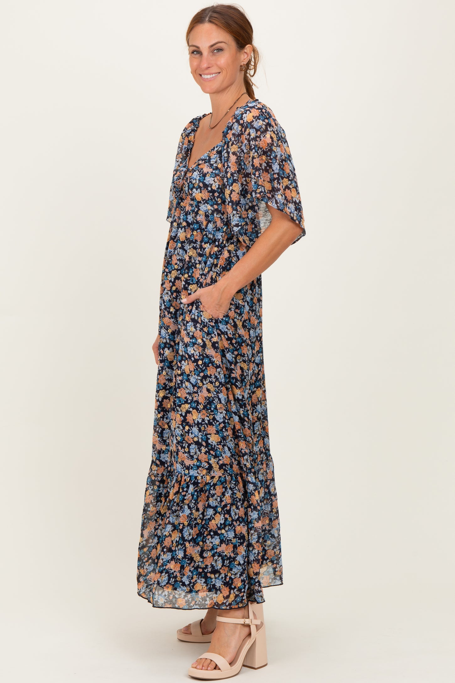woman wearing a navy floral maxi dress with short sleeves and side pockets, standing in profile