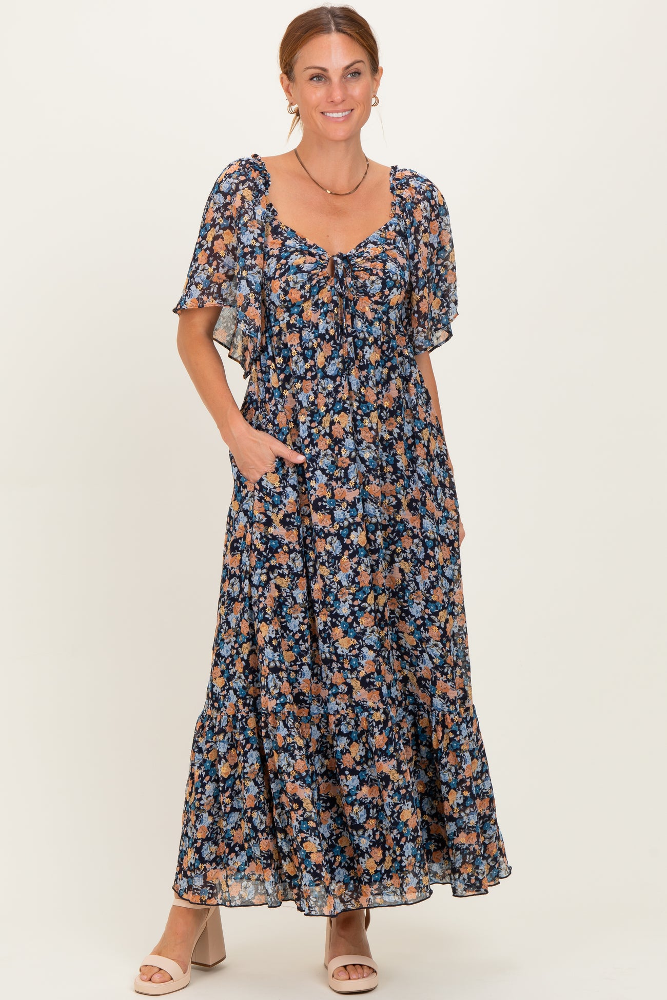 woman wearing a navy floral maxi dress with short flutter sleeves and pockets