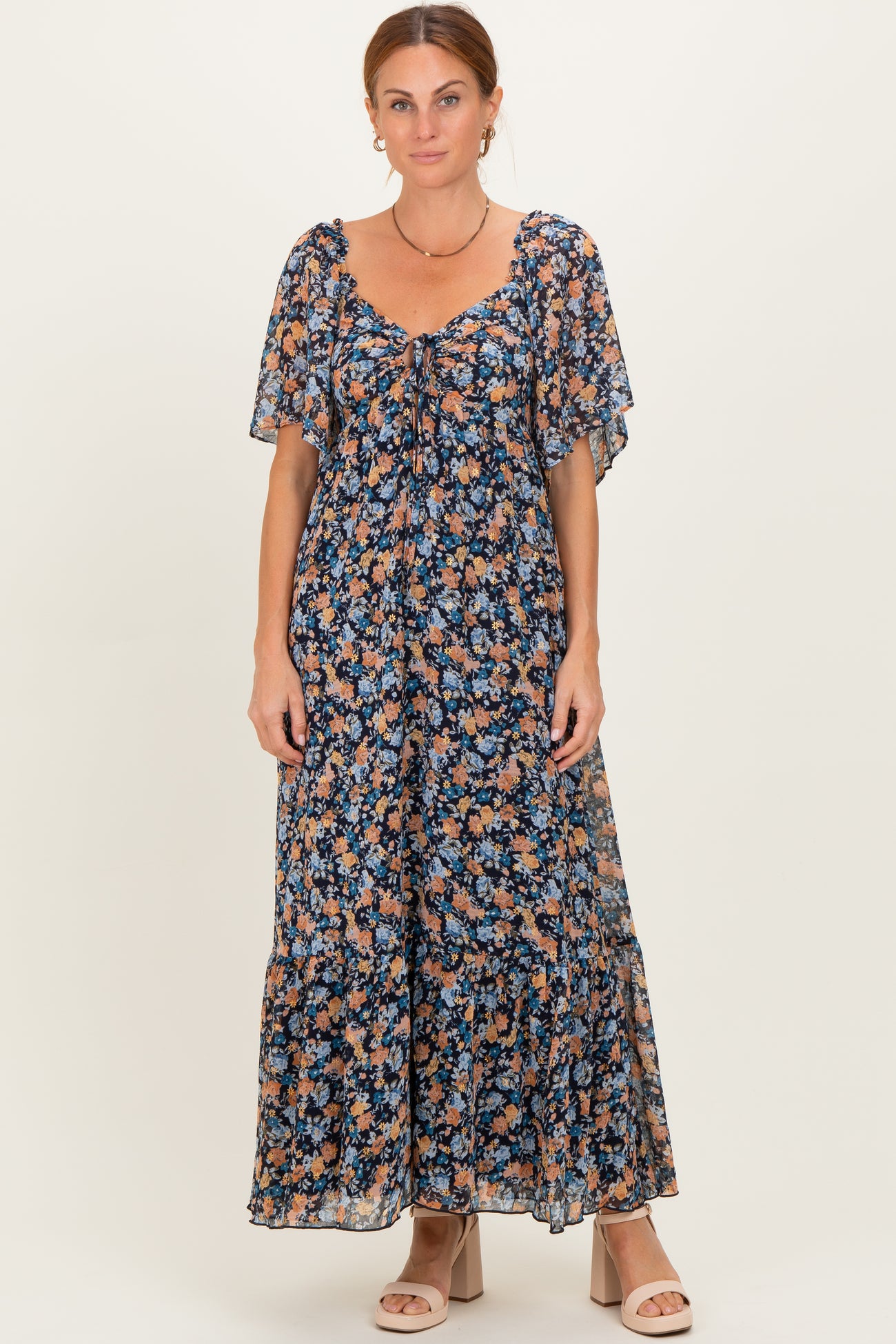 woman wearing a floral maxi dress with flutter sleeves and a tie front detail, standing against a light background