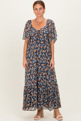 woman wearing a floral maxi dress with flutter sleeves and a tie front detail, standing against a light background