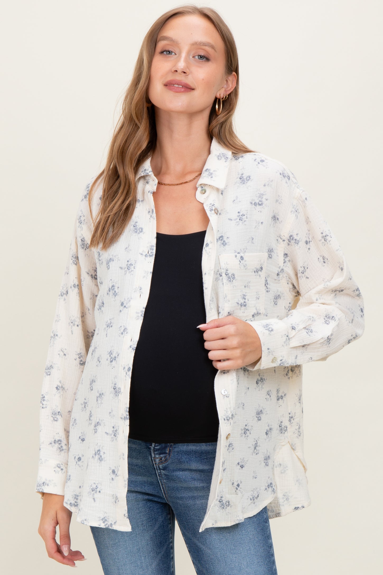 woman wearing a cream floral maternity button-up shirt and showing her baby bump with blue jeans