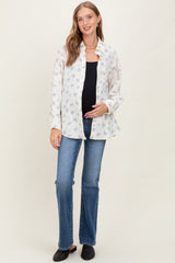 woman wearing a floral print maternity shirt over a black top and blue flared jeans, holding her baby bump