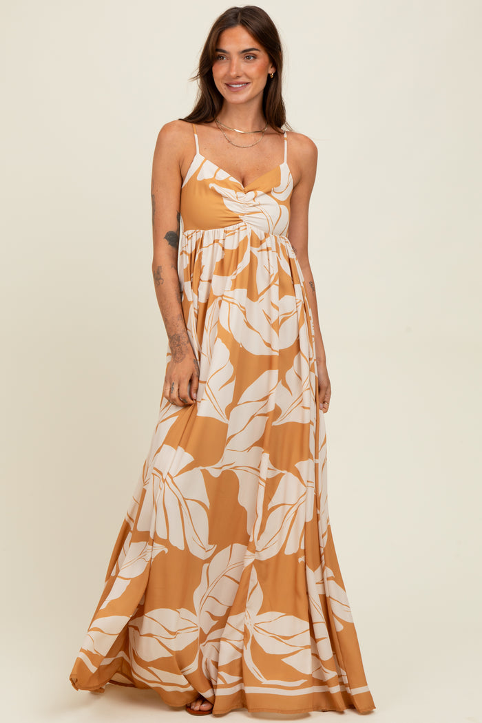 woman wearing a spaghetti strap maxi dress in amber with white leaf print and a twist front detail