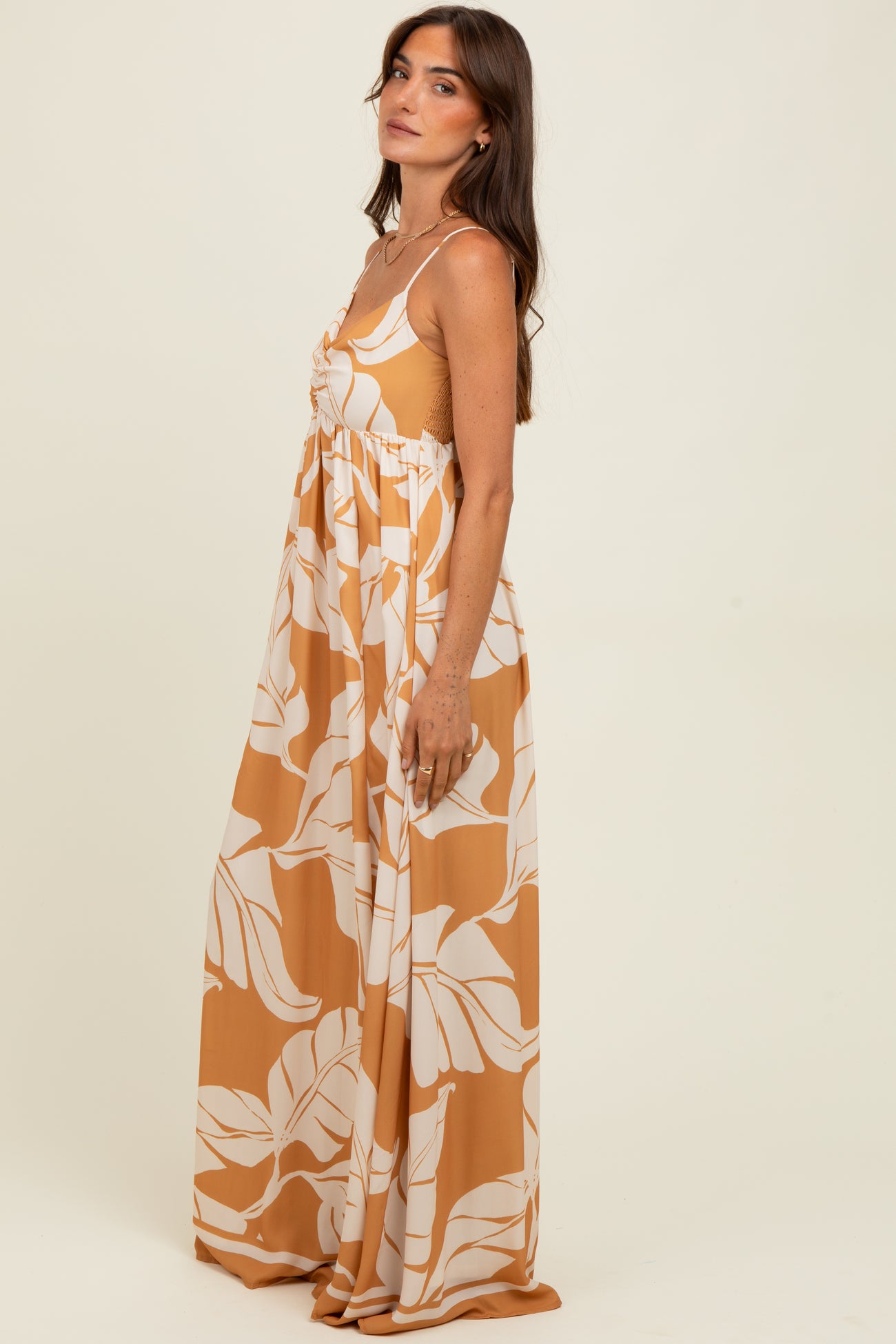 woman wearing a mustard yellow floral maxi dress with a fitted bodice and flowy skirt, standing sideways against a neutral background