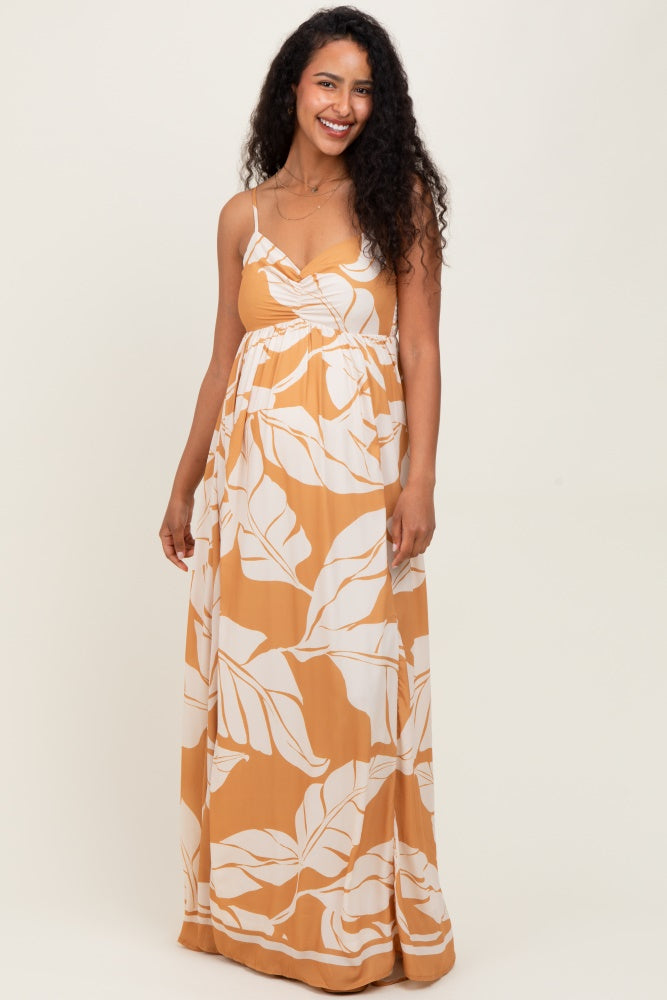 woman wearing a mustard yellow maternity maxi dress with white leaf patterns and spaghetti straps