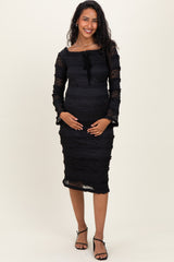 woman wearing a black lace maternity dress with three-quarter sleeves and a tie front, holding her baby bump