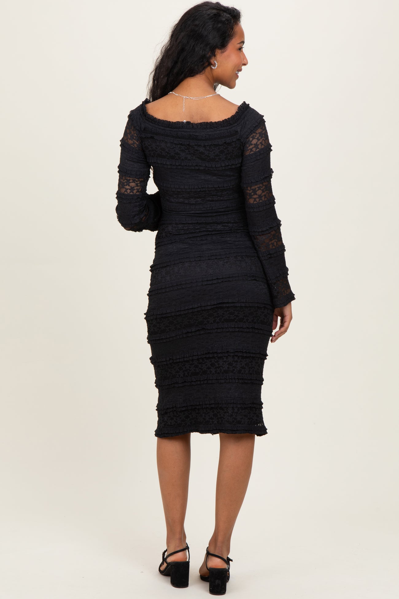 woman wearing a black lace maternity dress with long sleeves and a fitted silhouette, showing her baby bump from the back