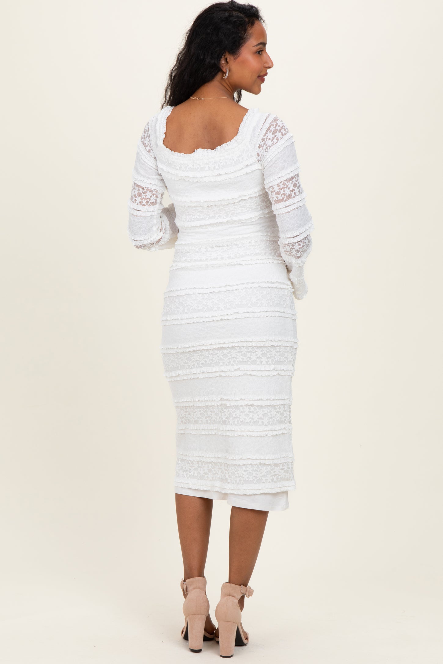 woman wearing a white lace maternity dress with long sleeves and a fitted silhouette, showing her baby bump from the back