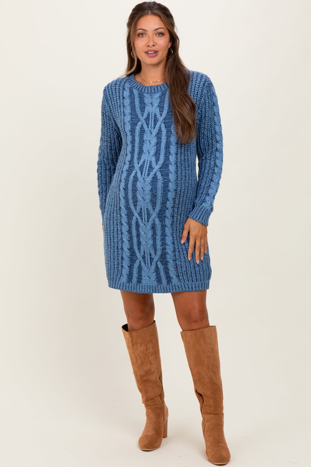 woman wearing a blue cable knit maternity sweater dress with long sleeves and knee-high brown boots, showing her baby bump