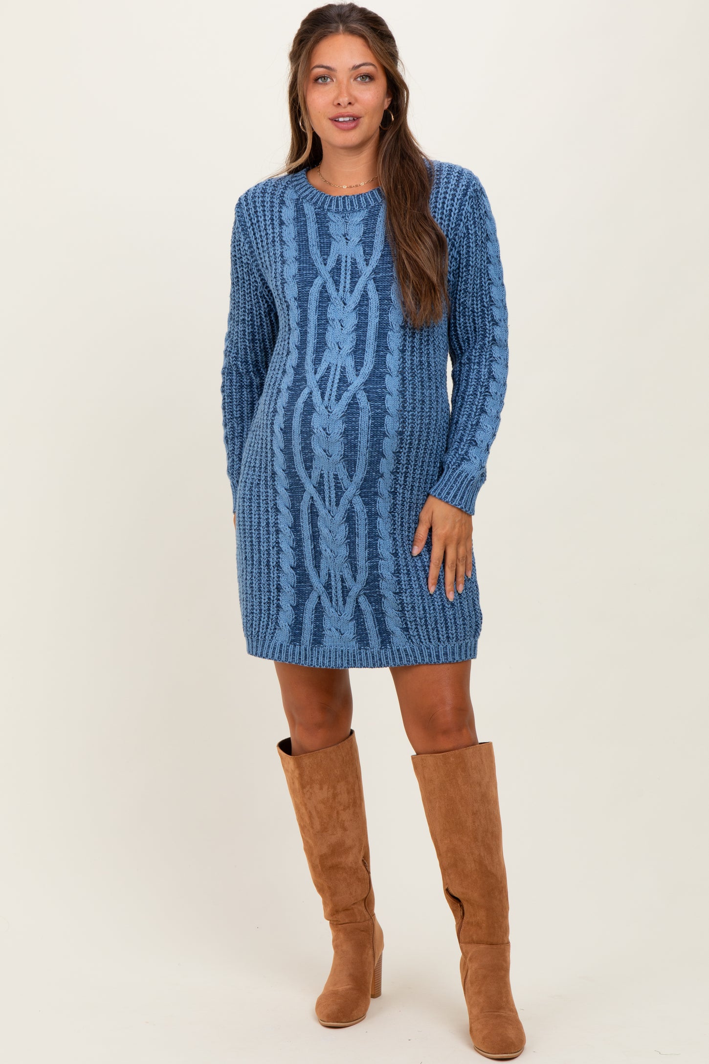 woman wearing a blue cable knit maternity sweater dress with long sleeves and knee-high brown boots, showing her baby bump