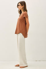 woman wearing a rust short sleeve tee with side slits and cream wide-leg pants sandals.
