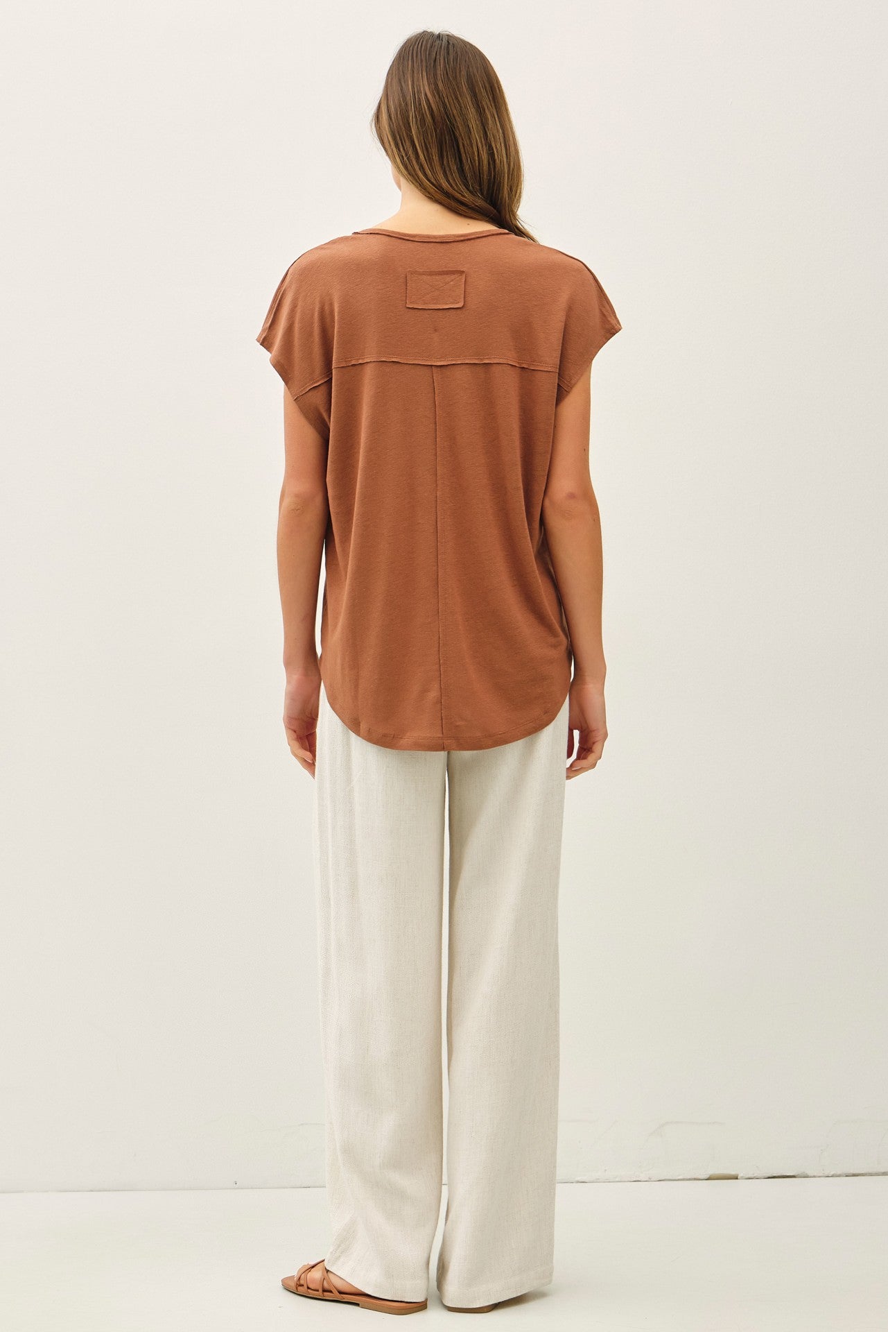 woman wearing a rust-colored short sleeve top with a back pocket and light beige wide-leg pants