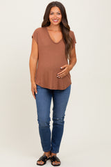 woman wearing a rust v-neck maternity top and blue jeans, holding her baby bump