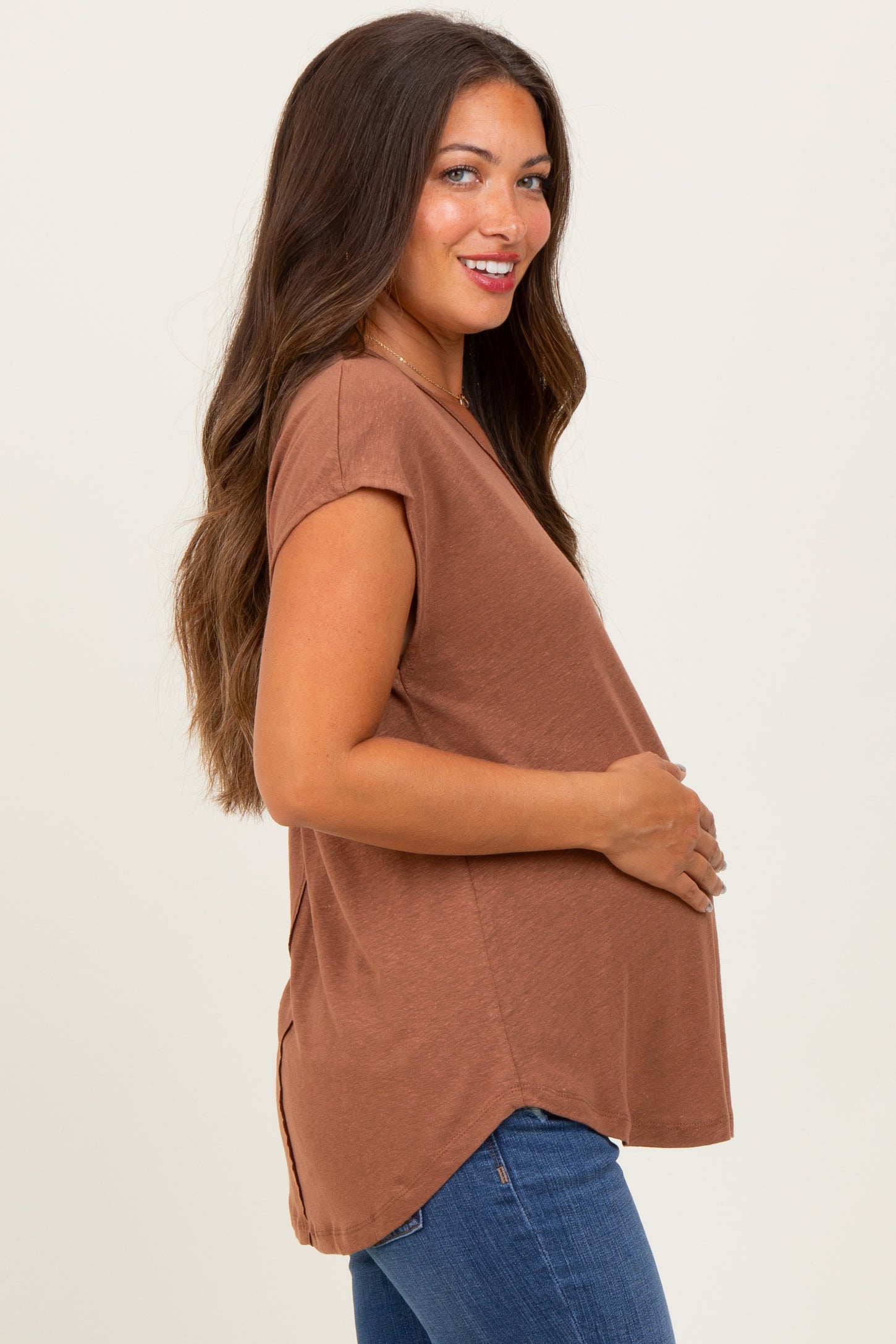 woman wearing a brown short sleeve maternity top and holding her baby bump